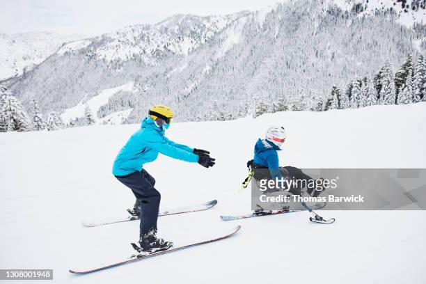 Full length view of friend giving female adaptive athlete on monoski a push while skiing at resort