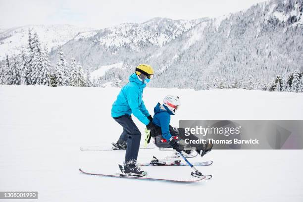 full length view of friend helping female adaptive athlete on monoski though flat area at ski resort - womens us ski team stock pictures, royalty-free photos & images