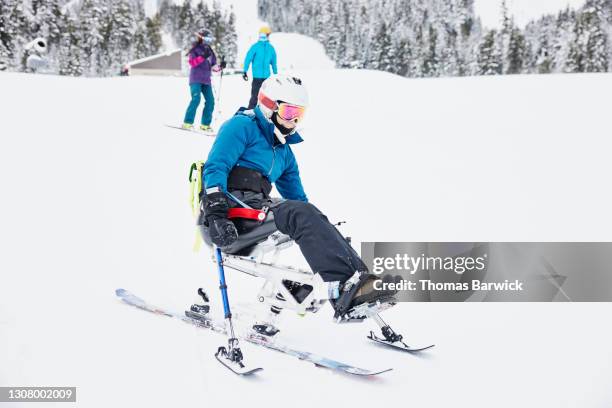 full length view of female adaptive athlete skiing on monoski with friends at ski resort on winter morning - disabilitycollection ストックフォトと画像