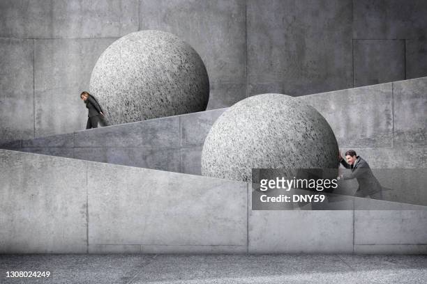 man and woman pushing large spheres up a concrete ramp - capitalism stock pictures, royalty-free photos & images