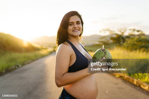 pregnant woman holding a coconut ready to drink - coconut water stock pictures, royalty-free photos & images