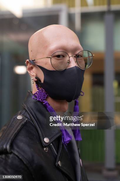 Guest is seen on the street wearing black leather jacket with pins, grey outfit, vintage brown leather bag, purple tassel earings, black face mask...