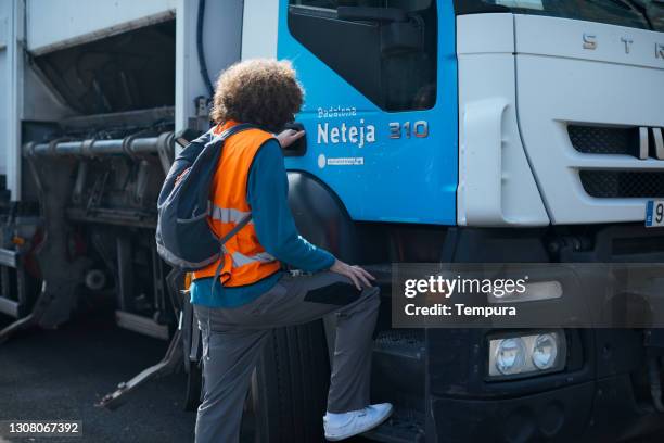 a garbage collector entering a trash truck. - garbage truck driving stock pictures, royalty-free photos & images