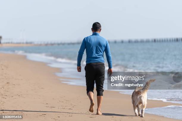 mens die op het strand met zijn hond loopt. - middle age man and walking the dog stockfoto's en -beelden