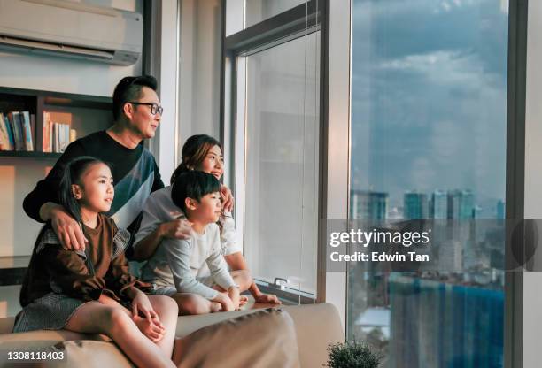 famiglia cinese asiatica con 2 bambini che guardano attraverso la finestra godendo di un bellissimo tramonto nel soggiorno nella città di kuala lumpur - apartment living asian foto e immagini stock