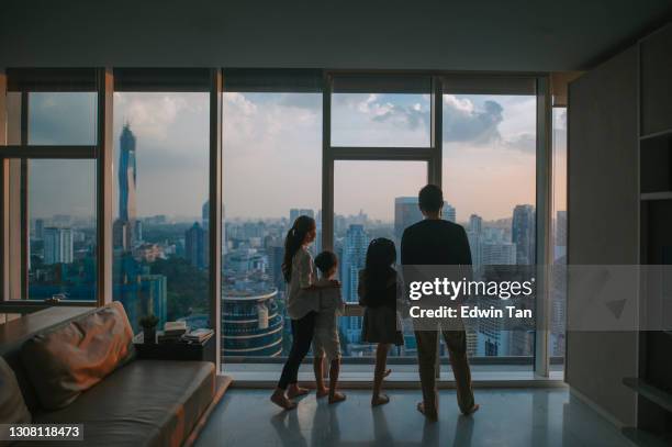 silhouette rear view  asian chinese family with 2 children looking through window enjoying beautiful sunset at living room in kuala lumpur city - family rear view stock pictures, royalty-free photos & images