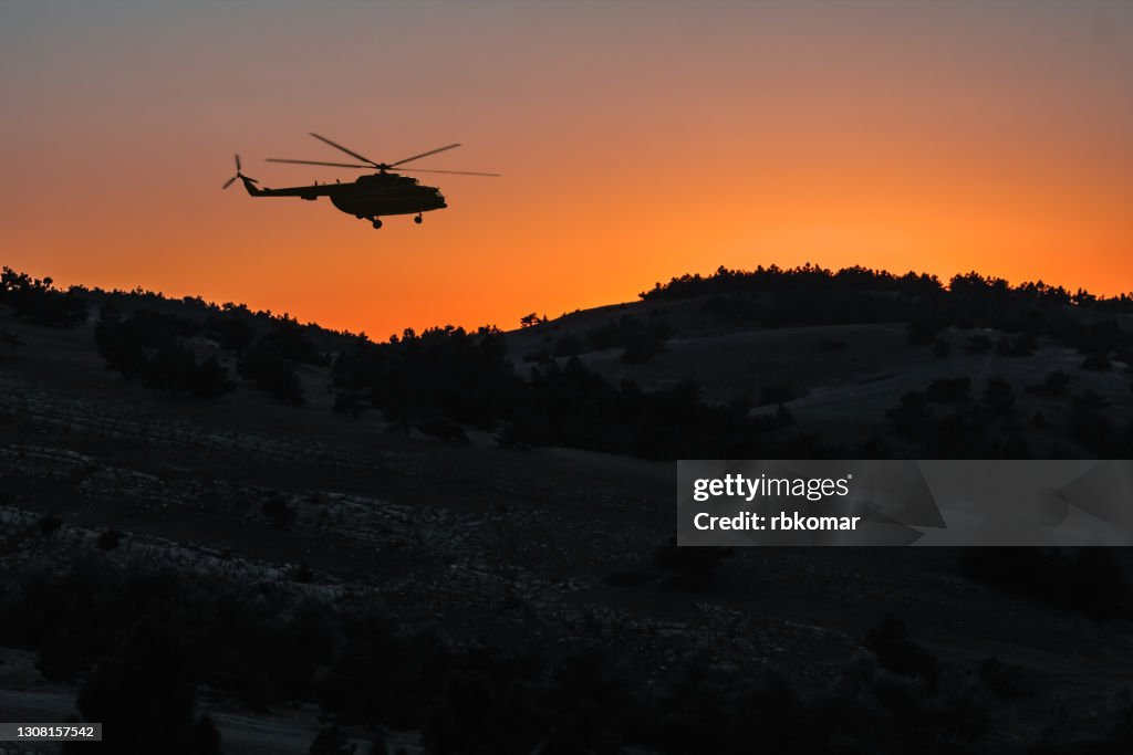 Silhouette of a rescue helicopter flying over the mountains at night at sunset. A military transport helicopter landing at a remote location in the hills. Accident and urgent search operation