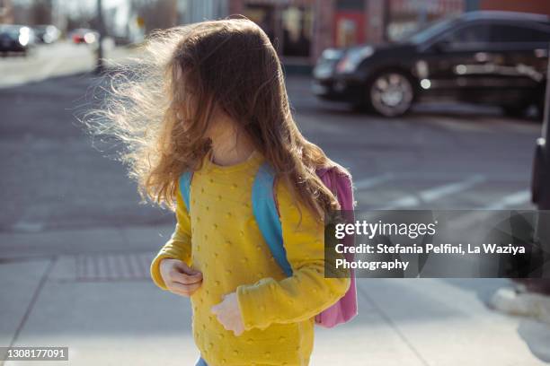 little girl wearing a backpack is standing on a sidewalk near a crossroad - cross road children stockfoto's en -beelden