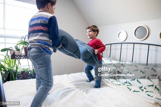 los niños pequeños tienen una pelea de almohadas mientras juegan juntos en el dormitorio - a boy jumping on a bed fotografías e imágenes de stock