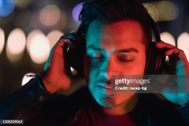 young and handsome indian man lit by neon lights and listening to music with headphones - indian art culture and entertainment stock pictures, royalty-free photos & images