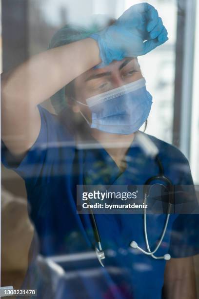 female young health care worker looking through a window - tired healthcare worker stock pictures, royalty-free photos & images