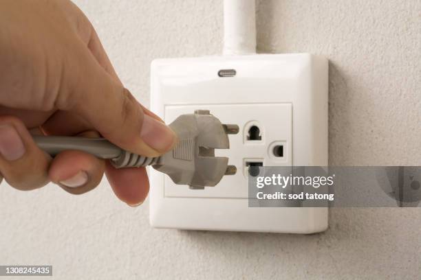 male hand puts plug in the socket, closeup shot - electrical overload stockfoto's en -beelden