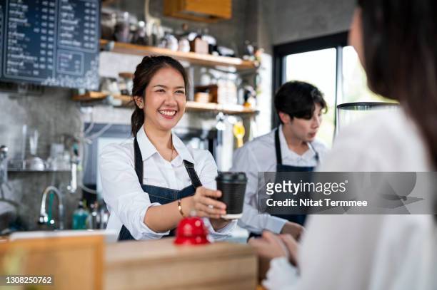 shot of a female barista serving a cup of coffee to a customer in a cafe counter. small business owner, service mind and customer service. - small business people working in asia stock-fotos und bilder
