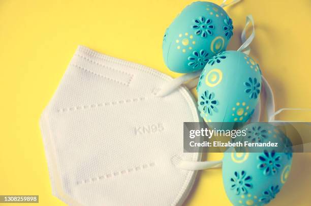 easter eggs and protective facial mask on yellow background. easter in pandemic time concept - easter mask stock-fotos und bilder