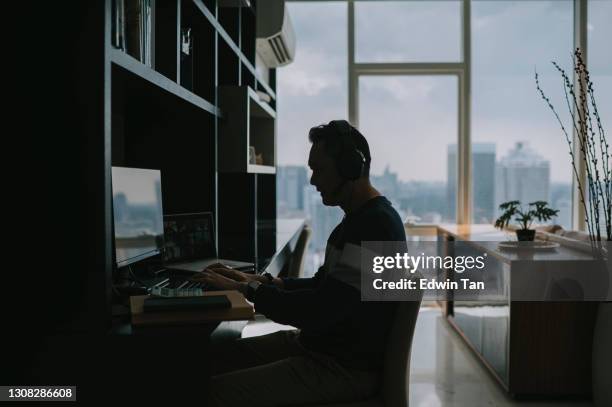 in silhouet zijaanzicht aziatische chinese volwassen man die vanuit huis werkt in woonkamer videogesprek met zijn collega - lifehack stockfoto's en -beelden