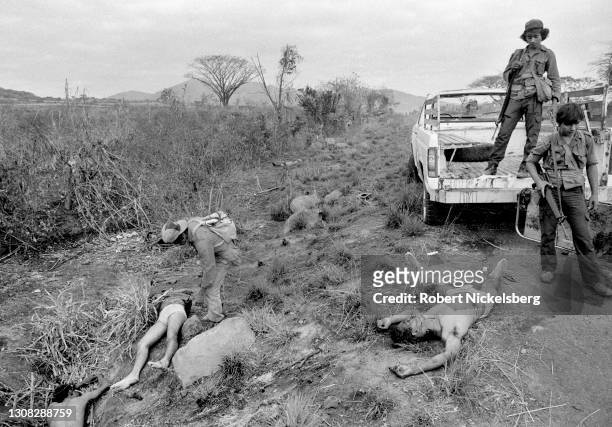 Two Fuerzas Populares de Liberacion guerrillas stand beside the corpses of several dead Salvadoran Army soldiers laying alongside a highway, near...