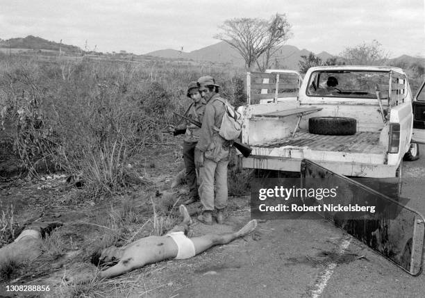 Two Fuerzas Populares de Liberacion guerrillas stand beside the corpses of several dead Salvadoran Army soldiers laying alongside a highway, near...