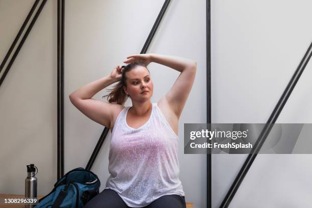vacker plusstorlek kvinna i sportkläder sitter i omklädningsrummet och binder håret i en hästsvans - locker room bildbanksfoton och bilder