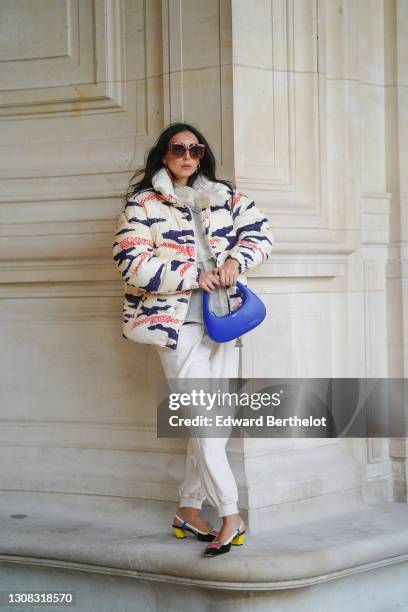 Gabriella Berdugo wears sunglasses, a white mesh lavalliere, a printed white blue and pink zebra pattern winter puffer coat from Moncler, beige...