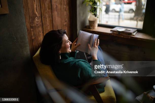 beautiful woman sitting in chair and reading a book. - season 1 stock-fotos und bilder