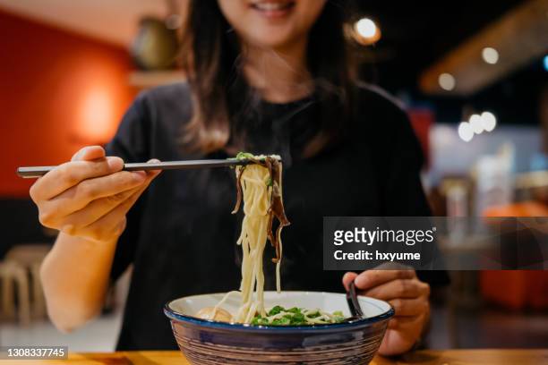 young woman eating a bowl of japanese ramen with chopsticks - ramen noodles stock pictures, royalty-free photos & images