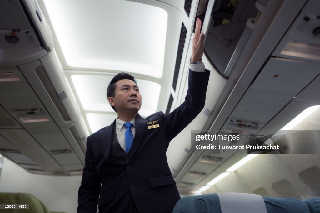 Confident Asian male pilot in uniform standing at the passenger seat inside of the airplane .