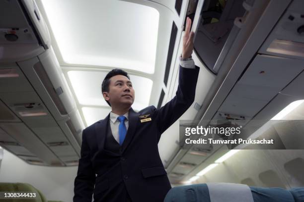 confident asian male pilot in uniform standing at the passenger seat inside of the airplane . - crew stock pictures, royalty-free photos & images