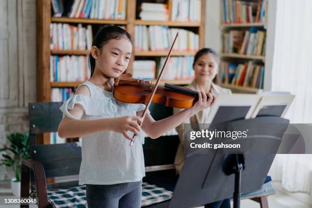 young girl playing violin near window in music school - young violinist stock pictures, royalty-free photos & images