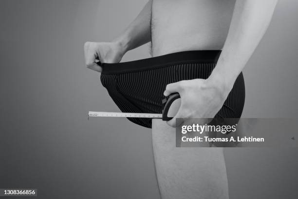 adult caucasian man pulling his boxers with a hand, holding a tape measure in other hand. - foreskin stock pictures, royalty-free photos & images