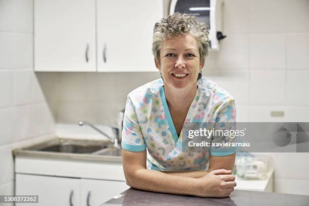 indoor portrait of cheerful female veterinarian in exam room - leaning on elbows stock pictures, royalty-free photos & images