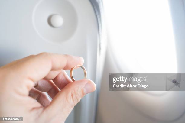 man's hand holding a gold wedding ring by an airplane window. - plane crush stock pictures, royalty-free photos & images