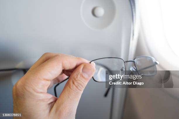 man's hand holding glasses next to an airplane window while seated. - lesebrille stock-fotos und bilder