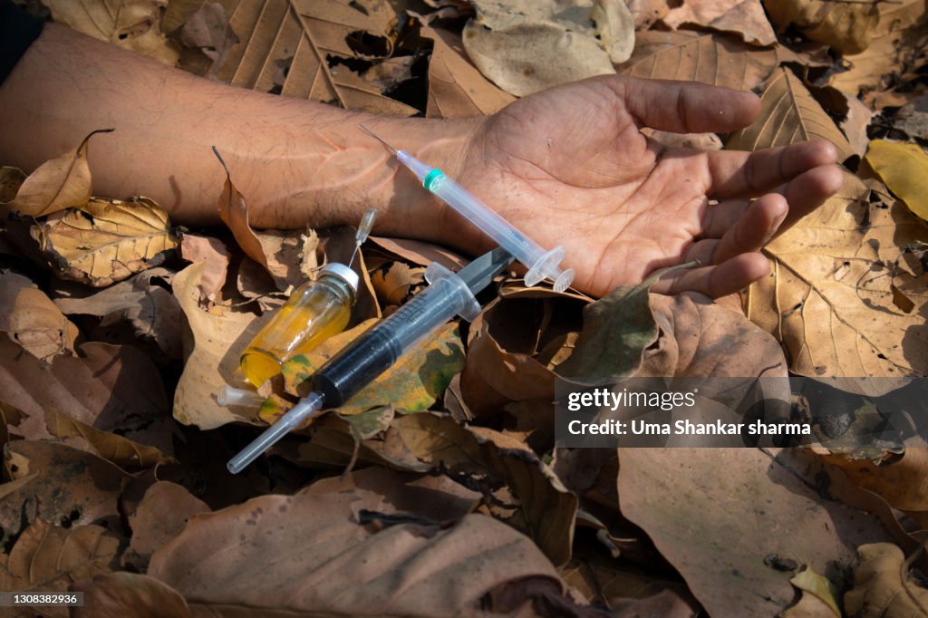 A drugged guys hand with syringe and injection as he is fainted due to overdose.