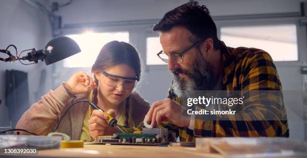 father assisting his daughter repairing motherboard with soldering iron - soldered stock pictures, royalty-free photos & images