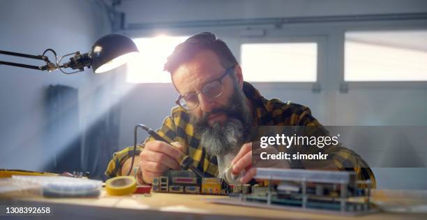 mature man using soldering iron on mother board - soldered stock pictures, royalty-free photos & images