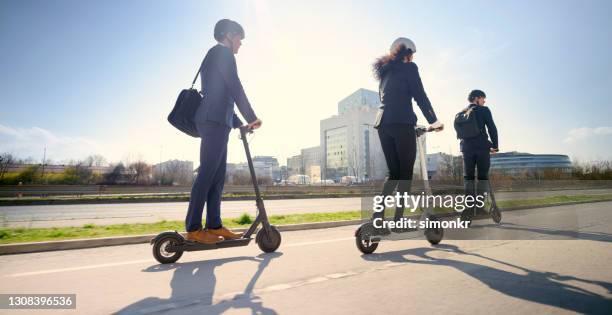 empresarios montando patinete eléctrico en la ciudad - mobility scooter fotografías e imágenes de stock