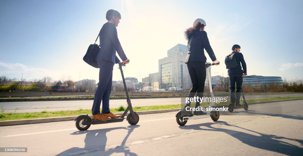 Bedrijfs mensen die elektrische duwscooter in stad berijden