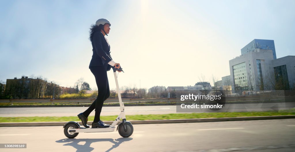 Zijaanzicht van rijpe vrouw die elektrische duwscooter in stad berijdt