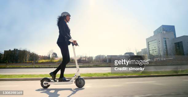 zijaanzicht van rijpe vrouw die elektrische duwscooter in stad berijdt - mobiliteit stockfoto's en -beelden
