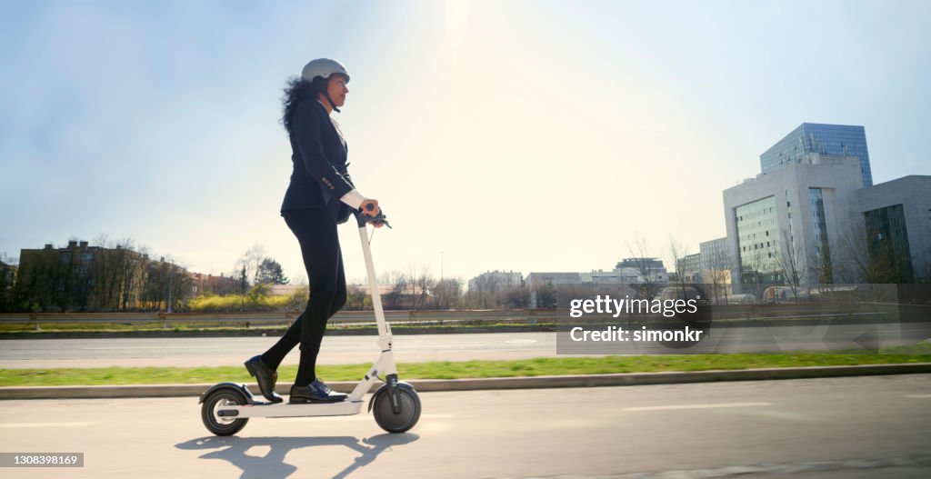 Side view of mature woman riding electric push scooter in city