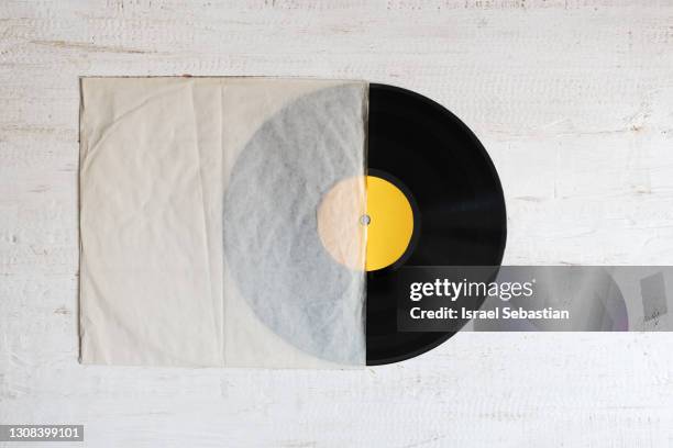 top view of a vintage vinyl record half out of its old paper sleeve, on a white wooden background. retro style - vintage record player no people ストックフォトと画像