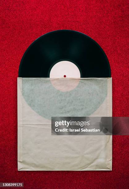 top view of a vintage vinyl record half out of its old paper sleeve, on a red background with glitter. retro style - garment tag stock pictures, royalty-free photos & images