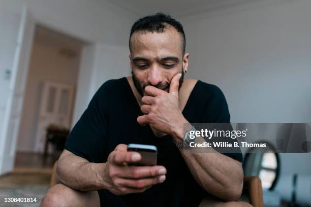 gay man reading messages on dating app with smartphone - sonrisa satisfecha fotografías e imágenes de stock