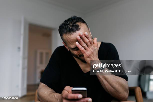 man with hand over his face while reading messaged on smartphone - touching head stock pictures, royalty-free photos & images