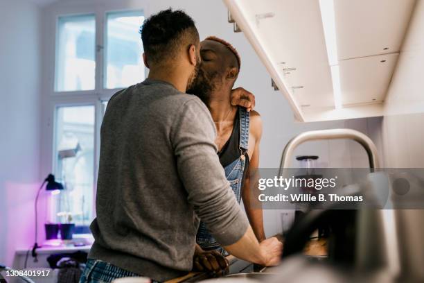 two men kissing while standing in kitchen together - black couples kissing stock pictures, royalty-free photos & images
