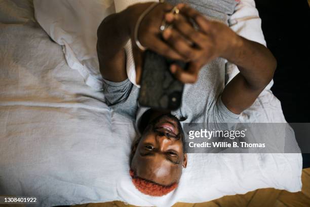 man smiling while laying on bed messaging using smartphone - men phone stock-fotos und bilder