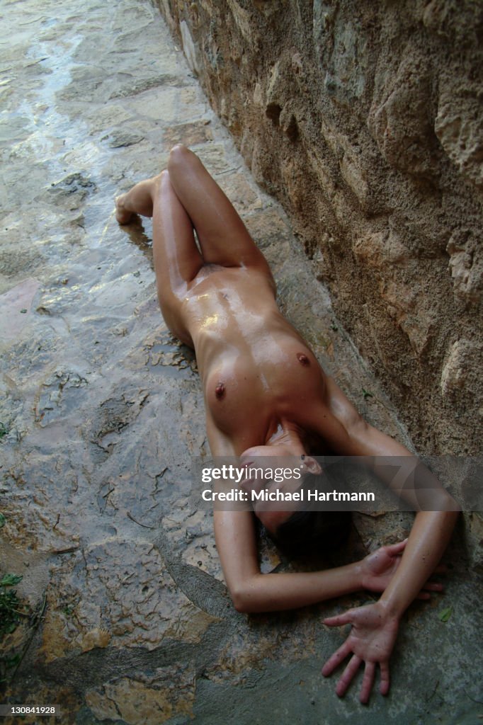 Naked young woman lying on a natural stone path refreshing her skin with water, Majorca, Spain