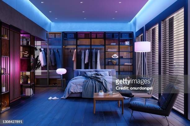 modern slaapkamerinterieur 's nachts met neonlicht. rommelig bed, kleding in kast, fauteuils en vloerlamp. - verlicht stockfoto's en -beelden