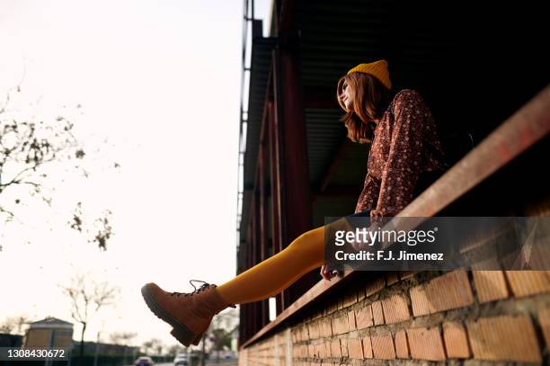 red-haired woman sitting on brick wall - nylon stock pictures, royalty-free photos & images