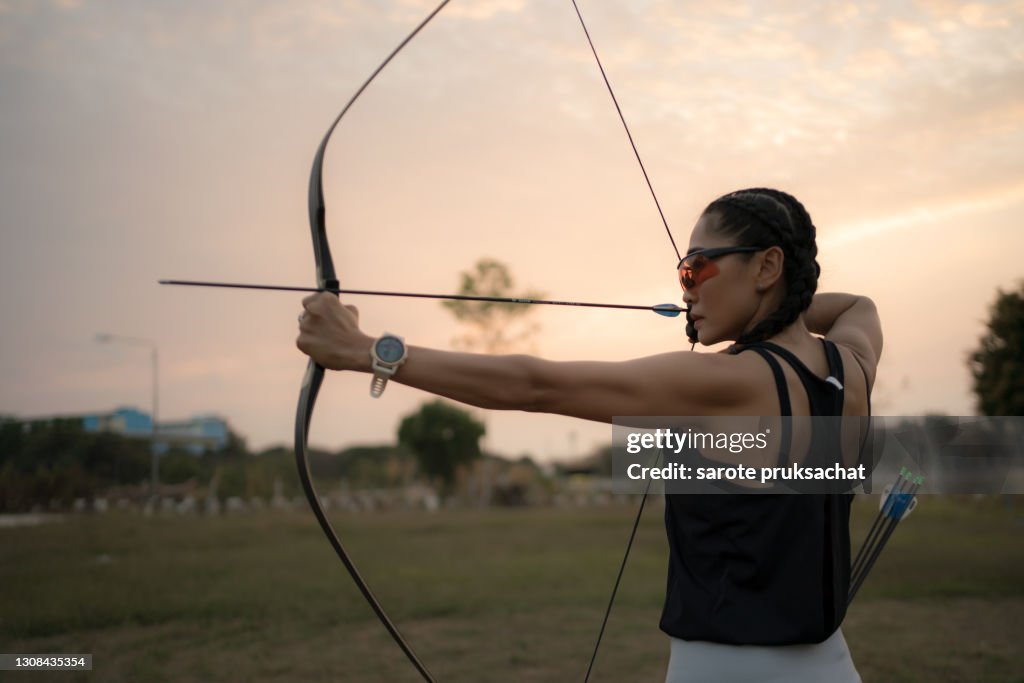 Rear view of sportswoman doing archery on a sports field against sunset .